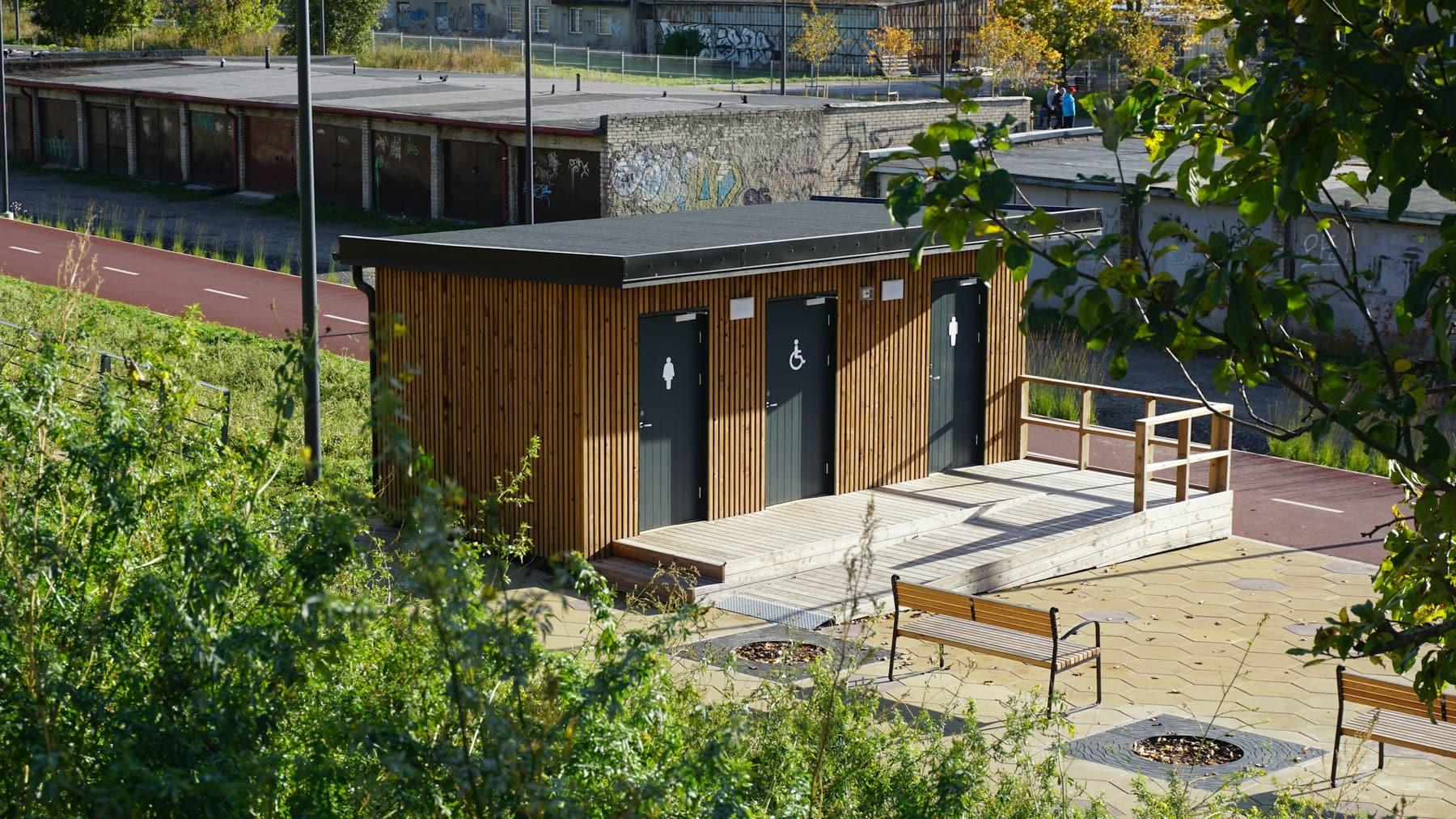 Single-storey restroom building with three doors and timber cladding beside a paved area